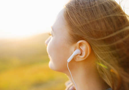 Young woman enjoying a music in the fall season. Autumn outdoor portrait.