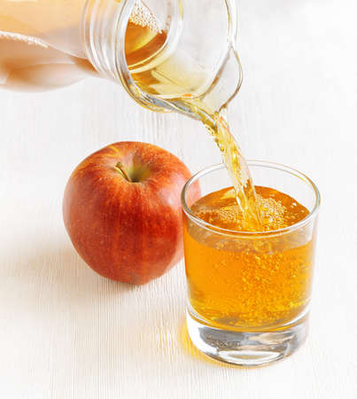 Apple juice pouring from jug into a glass.