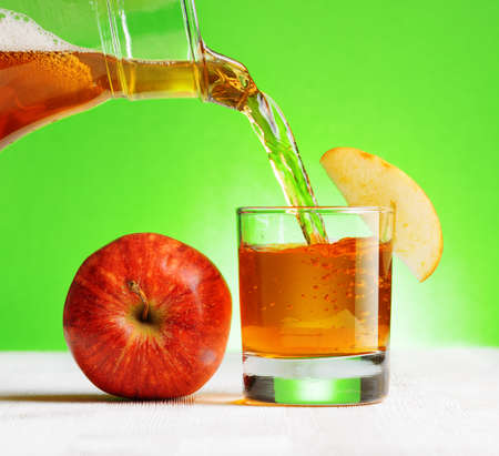 Apple juice pouring from jug into a glass. Green background.