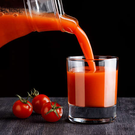 Tomato juice pouring from jug into a glass. Black background.の写真素材
