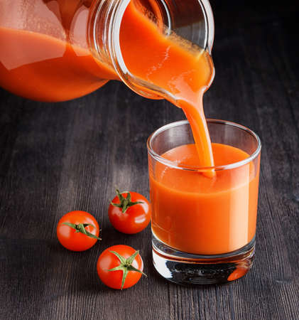 Tomato juice pouring from jug into a glass.の写真素材