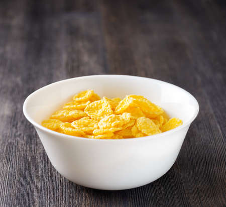 Bowl of cornflakes on wooden table.