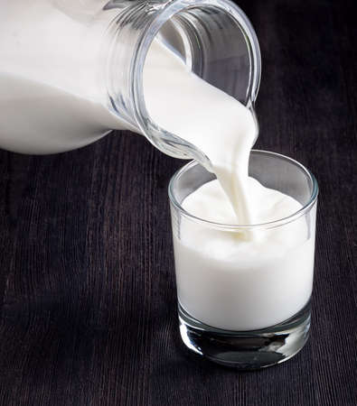 Milk pouring into a glass on black board.の写真素材