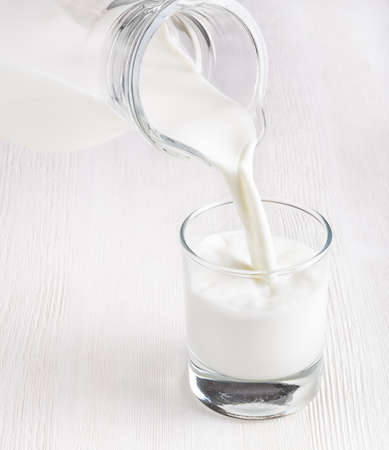 Milk pouring into a glass on white board.の写真素材