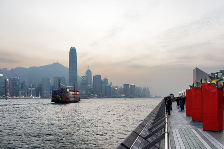Tourist boat in Victoria harbor and the view of skyscrapers from Avenue of Stars on waterfront in...