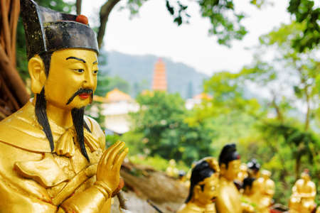 Closeup view of Golden Buddha statue in the Ten Thousand Buddhas Monastery on background of a red pagoda and forest in Hong Kong. Hong Kong is popular tourist destination of Asia.の写真素材