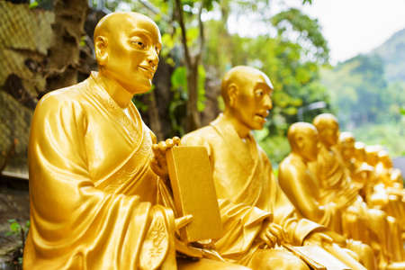 Golden Buddha statues along the stairs leading to the Ten Thousand Buddhas Monastery and beautiful forest landscape in the background in Hong Kong. Hong Kong is popular tourist destination of Asia.の写真素材