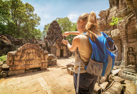 Closeup view of young female tourist with smartphone taking picture of the bas-relief under blue sky among mysterious ruins of Preah Khan temple in Angkor. Siem Reap, Cambodia. Toned image.の写真素材