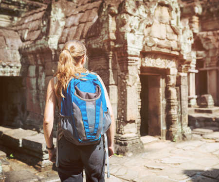 Young female tourist with blue backpack walking among mysterious ruins of ancient Preah Khan temple in Angkor. Siem Reap, Cambodia. Toned image.の写真素材
