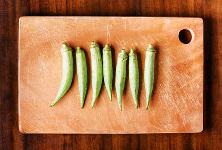 Top view of fresh green seed pods okra on a wooden board on a table. Healthy eco food rich in vitamins, folate, antioxidants, calcium and potassium. Popular product of organic farming in Asia.の写真素材