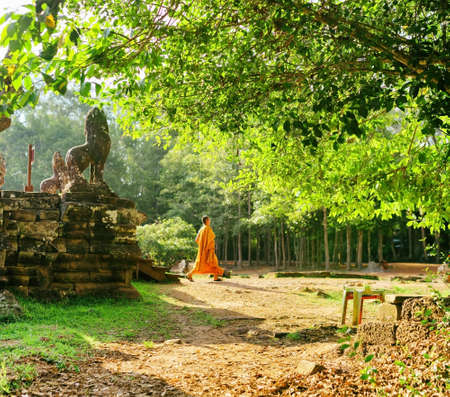 Green tree near mysterious ruins of ancient Bayon temple in Angkor Thom. Buddhist monk coming out of temple in background. Siem Reap, Cambodia. Angkor Thom is a popular tourist attraction.の写真素材