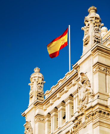 The flag of Spain fluttering on the Cybele Palace (Palacio de Cibeles) or the Palace of Communication in Madrid, Spain. Blue sky in background. Madrid is a popular tourist destination of Europe.のeditorial素材