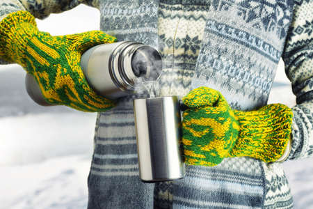 Woman is pouring a hot drink in mug from thermos.の写真素材