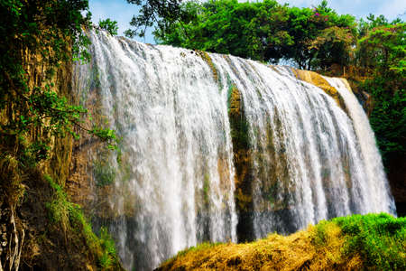 Amazing waterfall with crystal clear water among green woods on blue sky background in Vietnam. Beautiful summer sunny forest landscape. The Elephant waterfall is a popular tourist destination of Asiaの写真素材