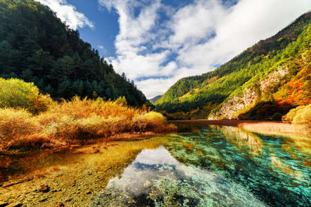 Amazing crystal clear water of river among mountains in autumn, Jiuzhaigou nature reserve (Jiuzhai Valley National Park), China. Evergreen woods in background. Beautiful colorful fall landscape.の写真素材