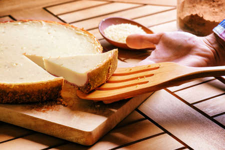 Hand taking piece of delicious freshly baked cheesecake. Homemade sweet dessert on wooden table, family meal.の写真素材
