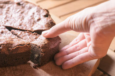 Closeup view of hand taking piece of freshly baked chocolate brownie cake with walnuts. Homemade...