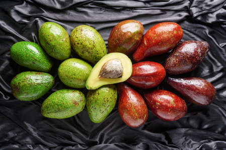 Top view of colorful fresh ripe avocado varieties on dark background. Green and red fruits....
