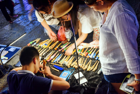 Guilin, China - September 19, 2017: Chinese artist making wooden carved souvenirs and female tourists choosing gifts at night market in Yangshuo Town. Yangshuo is a popular tourist destination of Asiaのeditorial素材