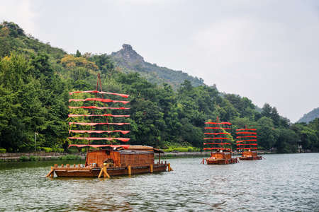 Amazing wooden ships decorated with red flags and parked on lake among green woods in Guilin, China. Guilin is a popular tourist destination of Asia.の写真素材