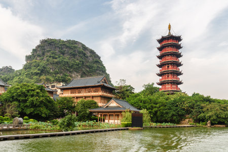Scenic red pagoda by the Mulong Lake (Wooden Dragon Lake) in Guilin, China. Beautiful wooded karst mountain is visible on blue sky background. Guilin is a popular tourist destination of Asia.のeditorial素材