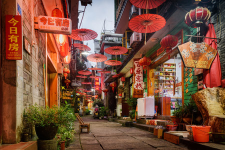 Fenghuang, China - September 22, 2017: Beautiful view of cozy narrow street decorated with traditional oriental Chinese red umbrellas in Phoenix Ancient Town (Fenghuang County) at evening.のeditorial素材