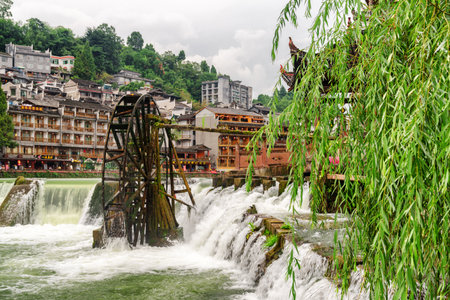 Fenghuang, China - September 22, 2017: Scenic view of water wheel and waterfall on the Tuojiang River in Phoenix Ancient Town. Beautiful green foliage of weeping willow is visible at right side.のeditorial素材
