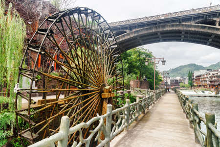 Scenic water wheel and bridge over the Tuojiang River (Tuo Jiang River) in Phoenix Ancient Town (Fenghuang County), China. Fenghuang is a popular tourist destination of Asia.の写真素材