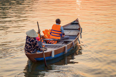 Tourist traveling by boat at sunset, Hoi An Ancient Town (Hoian), Vietnam. Vietnamese woman in traditional bamboo hat rowing on the Thu Bon River in evening.の写真素材