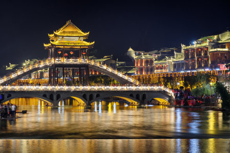 Fenghuang, China - September 22, 2017: Scenic night view of amazing bridge over the Tuojiang River (Tuo Jiang River) in Phoenix Ancient Town. Tourists walking along beautiful bridge.のeditorial素材