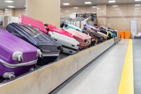 Violet and pink suitcases on luggage conveyor belt at arrival area of passenger terminal in airport. Baggage carousel.の写真素材