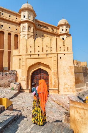 Jaipur, India - 12 November, 2018: Unknown Indian woman wearing traditional colorful sari holding child on scenic gate background. Awesome view of the Amer Fort and Palace (Amber Fort) in Rajasthan.のeditorial素材