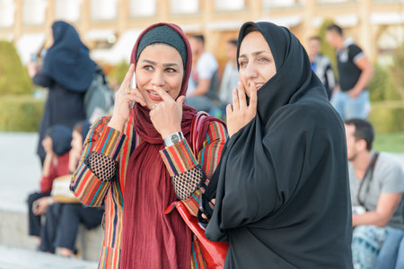 Isfahan, Iran - 24 October, 2018: Wonderful portrait of two pretty smiling Iranian women in Naqsh-e Jahan Square. One of women wearing traditional black chador.のeditorial素材
