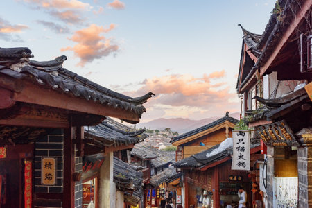 Lijiang, Yunnan Province, China - October 23, 2015: Awesome view of traditional Chinese black tile roofs of authentic houses in the Old Town of Lijiang. Scenic mountains are visible at sunset.のeditorial素材
