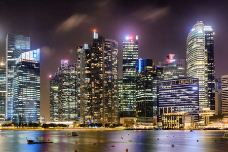 Awesome night view of downtown in Singapore. Amazing skyscrapers and other modern buildings on dark sky background. Colorful city lights reflected in water of Marina Bay. Beautiful cityscape.の写真素材