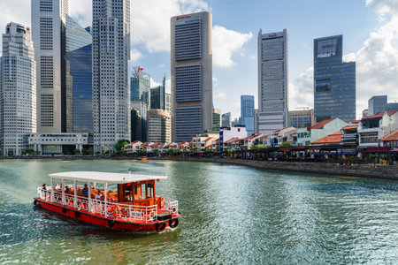 Singapore - February 19. 2017: Traditional tourist boat sailing along Boat Quay in Singapore. Amazing modern buildings are visible on blue sky background. Scenic summer cityscape.のeditorial素材