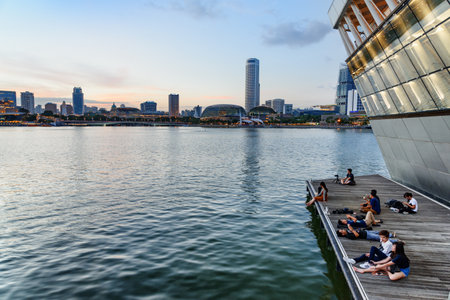 Singapore - February 17, 2017: Asian tourists rest on embankment of Marina Bay. Awesome Singapore skyline. Amazing evening cityscape. Singapore is a popular tourist destination of Asia.のeditorial素材