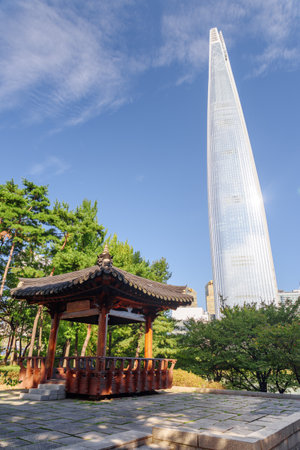 Scenic wooden pavilion of traditional Korean architecture among green trees and white skyscraper on blue sky background at downtown of Seoul, South Korea. Amazing summer sunny cityscape.のeditorial素材