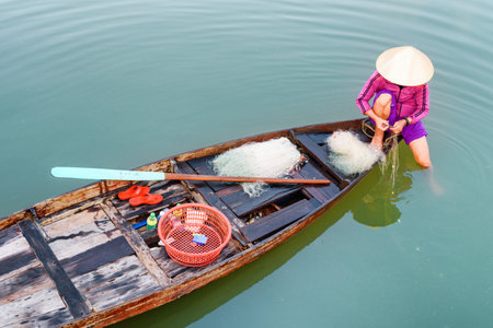 Amazing top view of Vietnamese woman in traditional hat on wooden boat checking her fishing net on the Thu Bon River at Hoi An Ancient Town, Vietnam. Hoian is a popular tourist destination of Asia.の写真素材