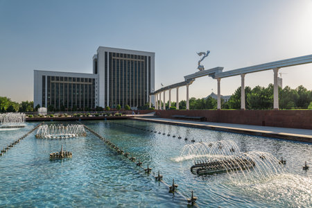 Awesome view of wonderful fountain in Mustaqillik Maydoni (Independence Square) of Tashkent, Uzbekistan. The Ministry of Tourism and Cultural and Storks Monument are visible on blue sky background.の写真素材