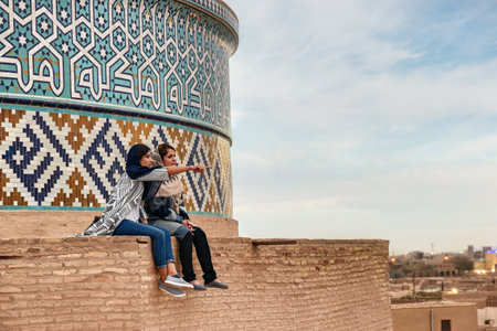 Yazd, Iran - 27 October, 2018: Two young Iranian women enjoy scenic view from the roof of the Jameh Mosque of Yazd. Beautiful mosaic of the dome. Azari style of Persian Islamic architecture.のeditorial素材