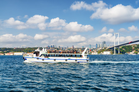 Tourist boat crossing the Bosporus. Awesome view of the Bosphorus Bridge (the 15 July Martyrs Bridge) connecting Europe to Asia. Amazing Istanbul skyline.の写真素材