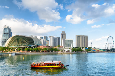 Beautiful view of traditional tourist boat sailing along Marina Bay with azure water in Singapore. Amazing modern buildings are visible on blue sky background. Scenic summer cityscape.の写真素材