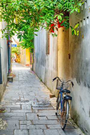 Scenic view of bicycle parked near wall of house on cozy narrow street in Hoi An Ancient Town (Hoian), Vietnam. Hoi An Ancient Town is a popular tourist destination of Asia.の写真素材