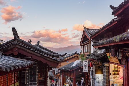 Lijiang, Yunnan Province, China - October 23, 2015: Awesome view of traditional Chinese black tile roofs of authentic houses in the Old Town of Lijiang. Scenic mountains are visible at sunset.のeditorial素材