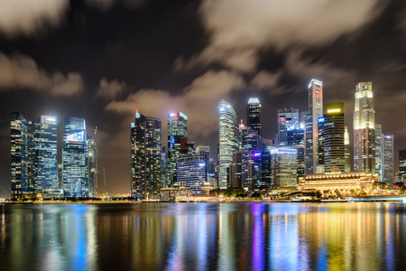 Awesome night view of downtown in Singapore. Amazing skyscrapers and other modern buildings on dark sky background. Colorful city lights reflected in water of Marina Bay. Beautiful cityscape.の写真素材