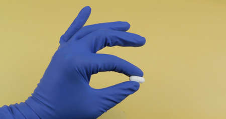 One oval white pill in hand dressed in rubber blue sterile medical glove. Concept of medicine and health improvement. Disease and the way of its treatmentの写真素材