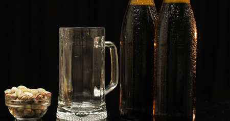 Two bottle of cold beer on a black background. A ray of light beautifully illuminates them. Empty...