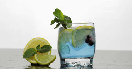 Glass with cold blue drink with leaves of mint, lime, lemon, black currants and ice cubes. Releasing...