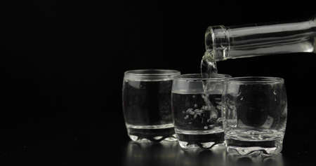 Pouring up shots of vodka from a bottle into glass against black background. Pour of alcohol drink...